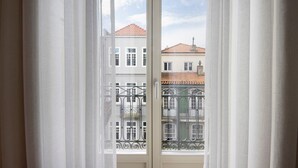 Una ventana con cortinas blancas, vista a edificios con balcones y cielo despejado.