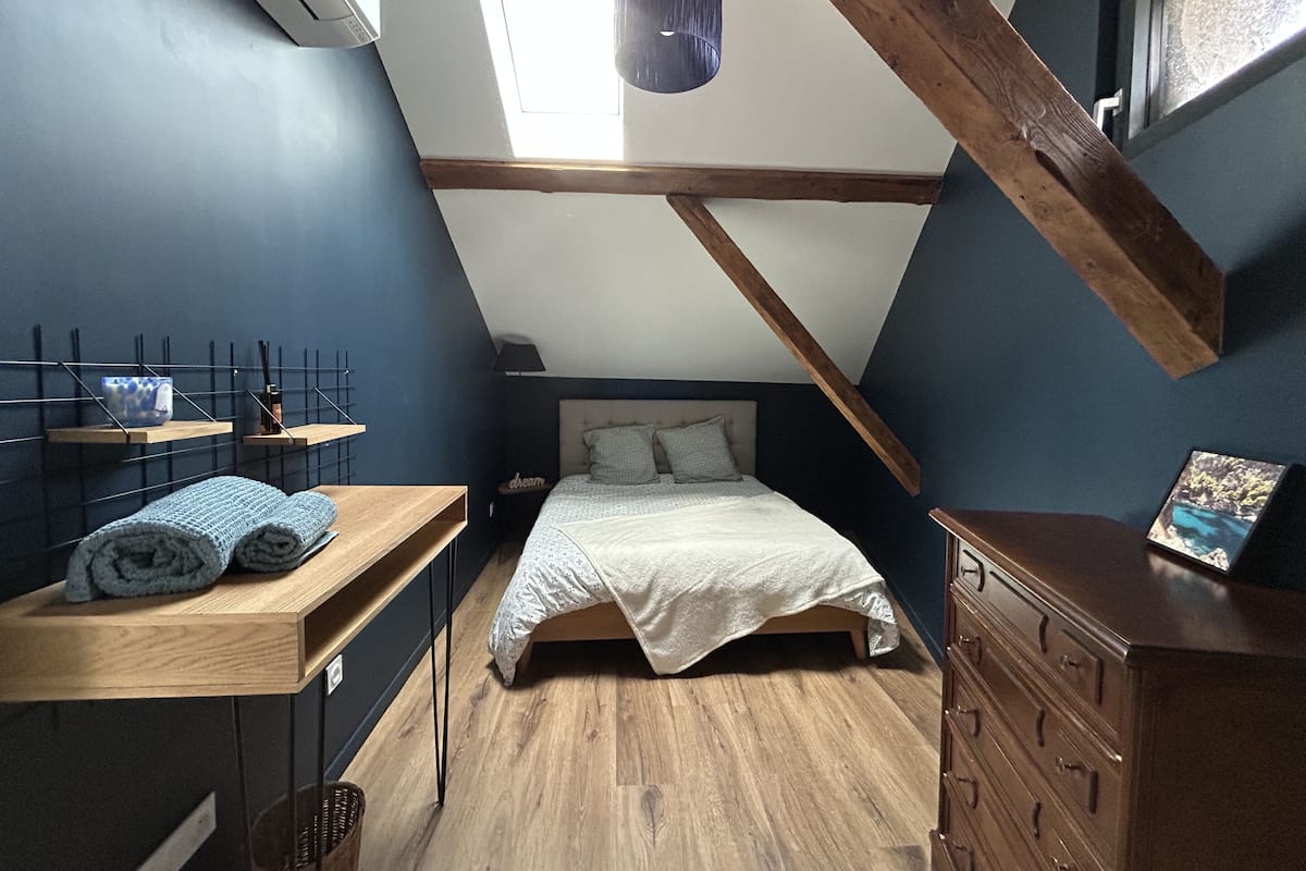 A small, cozy attic bedroom with a sloped ceiling, a bed, a dresser, and a small table with towels.