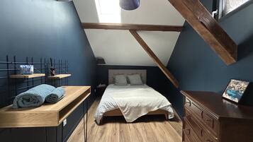 A small, cozy attic bedroom with a sloped ceiling, a bed, a dresser, and a small table with towels.