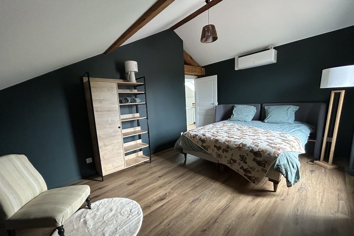 A bedroom with a bed, a chair, a wardrobe, and a bedside table.
