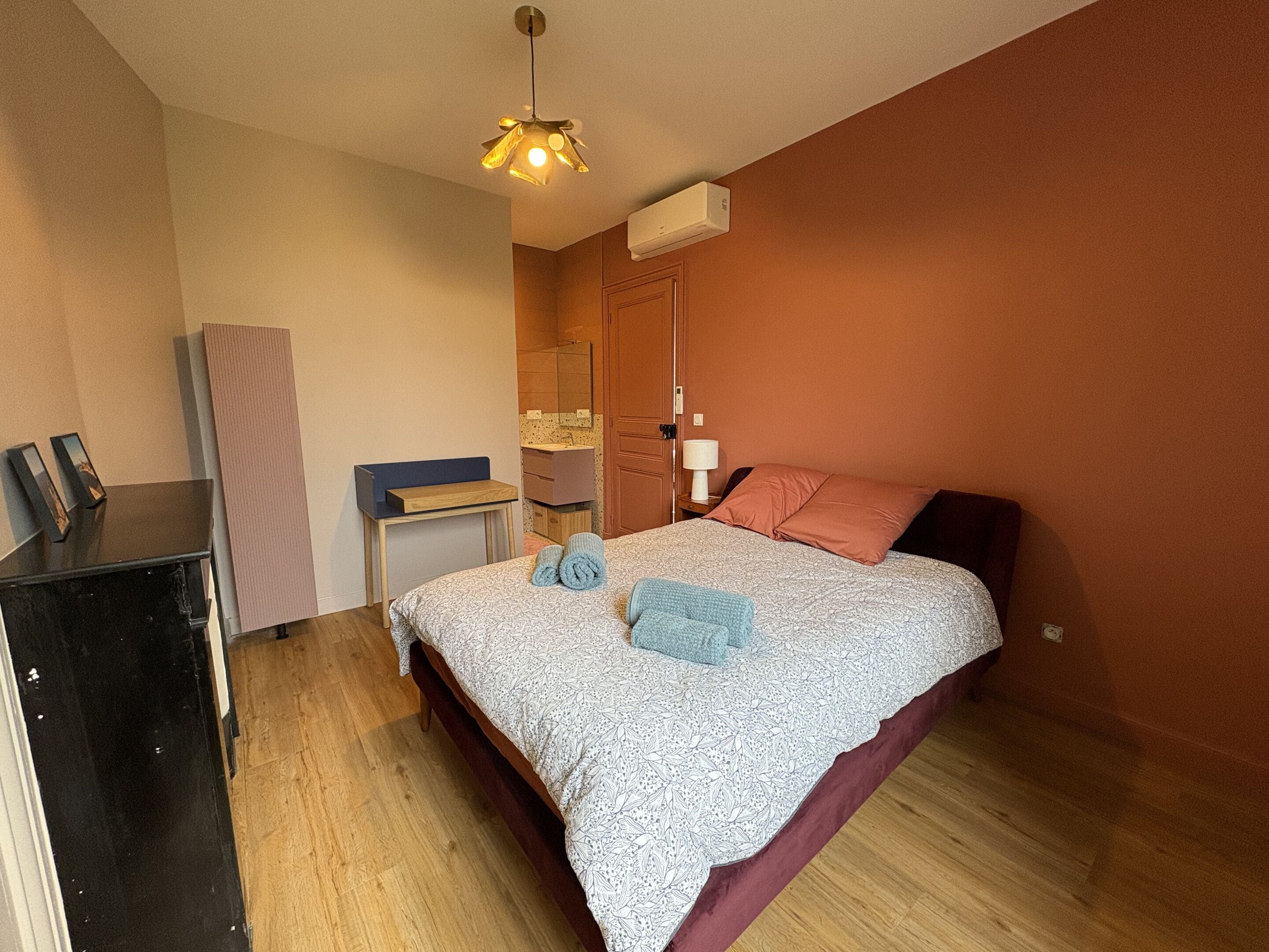 Un dormitorio con cama, mesita de noche, cómoda, espejo y lámpara colgante.