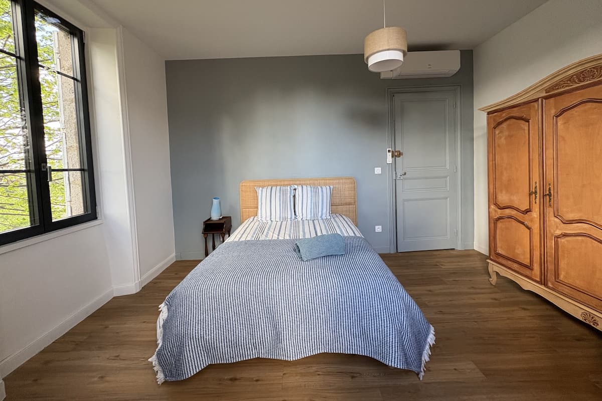 A bedroom with a bed, a nightstand, a wardrobe, a window, and a hanging light fixture.