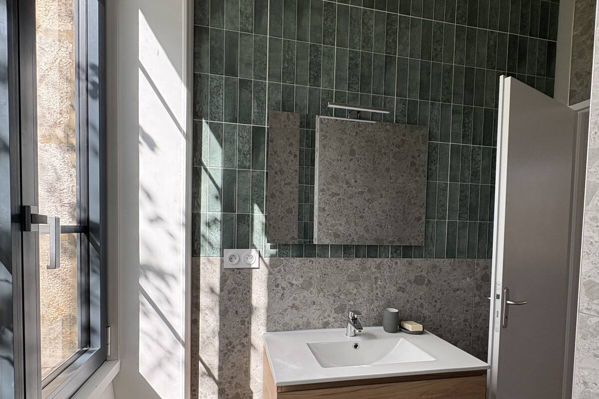 A bathroom with a white sink, wooden cabinet, and green tiled walls.