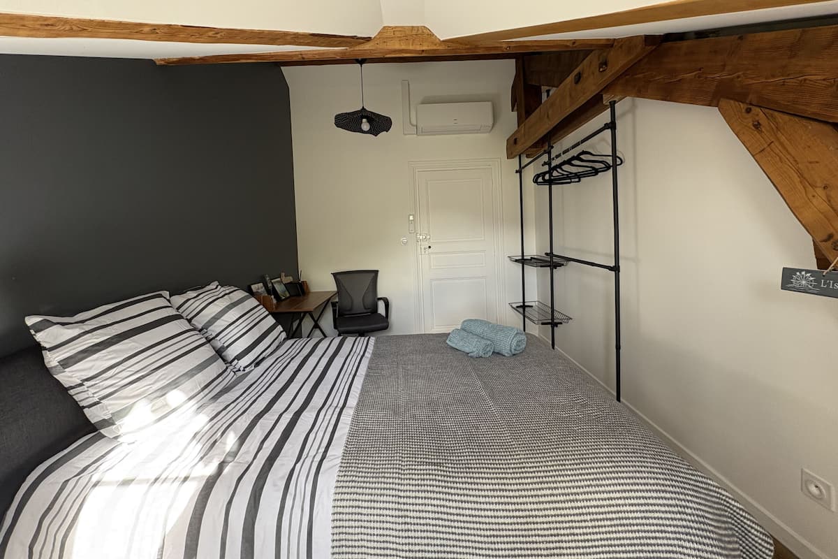 A bedroom with a bed, a chair, a desk, a coat rack, and a door.