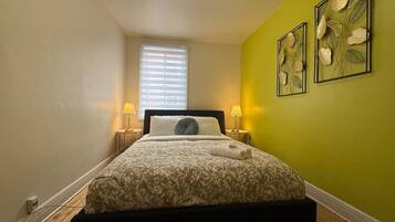 Un dormitorio con cama, lámparas de noche, ventana y pared verde.