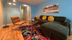 Ein Wohnzimmer mit einer Couch, einem Sessel, einem Couchtisch, einer Stehlampe und einem farbenfrohen Teppich.