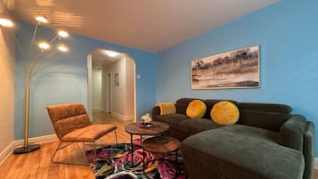 Una sala de estar con sofá, sillón, mesa de centro, lámpara de pie y una alfombra colorida.