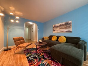 Una sala de estar con sofá, sillón, mesa de centro, lámpara de pie y una alfombra colorida.