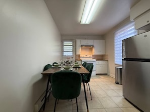 Una cocina compacta con una mesa de comedor preparada para cuatro personas, un refrigerador y una estufa.