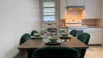 Un comedor con una mesa de madera dispuesta para cuatro personas, sillas verdes alrededor y una cocina al fondo.