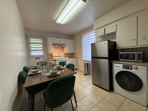 Une cuisine compacte avec un coin repas, équipée d’un four à micro-ondes, d’un réfrigérateur et d’un lave-linge.