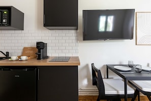 A modern kitchen with a built-in espresso machine, a coffee maker, and a tablet on the counter. - Studio de charme proche de la Gare Montparnasse (Paris)