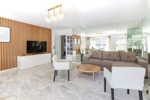 A modern living room with a flat-screen TV, a sofa, two chairs, and a coffee table. - Luxueux Appartement avec Terrasses à la Croisette (Cannes)