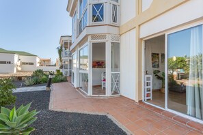Un edificio de varios pisos con un patio, amplias puertas correderas de vidrio y un pequeño espacio al aire libre con mesas y sillas.