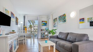 Un salon avec un canapé gris, une table basse blanche, un téléviseur et des œuvres d’art accrochées aux murs.