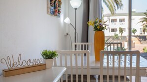 Une pièce avec une chaise blanche, une petite table sur laquelle est posé un panneau indiquant «Bienvenue», une plante en pot et un vase rempli de fleurs.