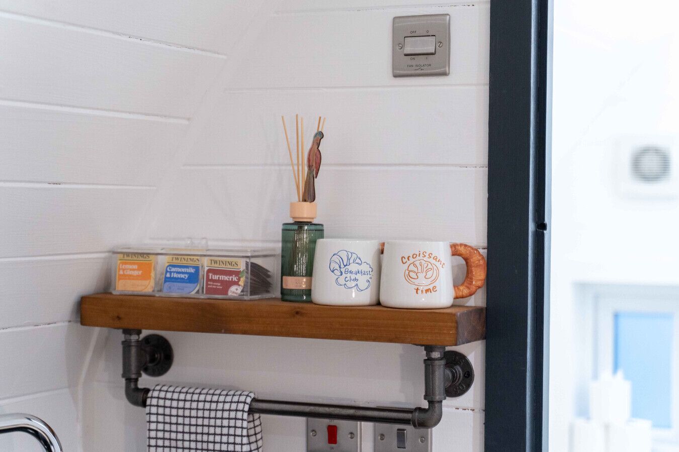 Un comptoir de cuisine avec une étagère où sont rangés les ustensiles essentiels, un ventilateur et une fenêtre.