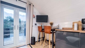 A modern kitchen with a large window, two stools, a coffee machine, and a trash bin. - Apex Studio Pod & Jacuzzi Bath (Fort William)