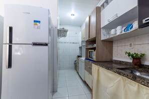 A kitchen with a white refrigerator, wooden cabinets, a microwave, and a sink. - Casa Climatizada a 400m da Praia no Centro (São Miguel dos Milagres)