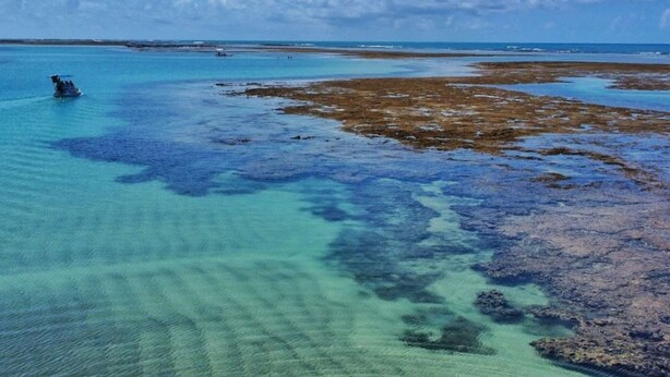 Vista aérea nítida de uma área costeira com águas rasas e um barco ao longe.
