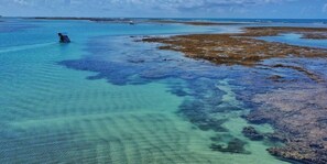 Vista aérea nítida de una zona costera con aguas poco profundas y un barco a lo lejos.