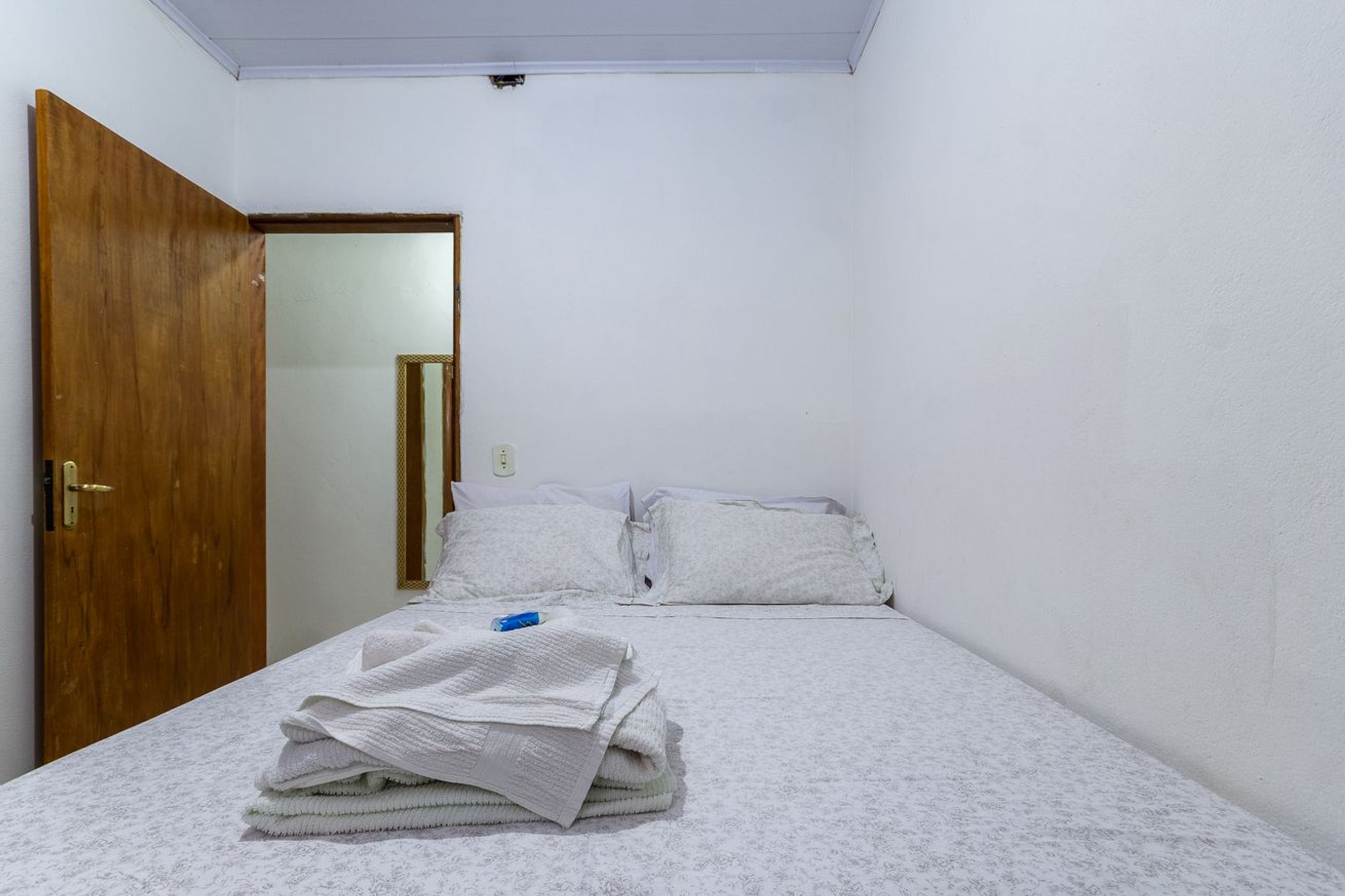 Une petite pièce propre, avec un lit, une porte en bois et un miroir.