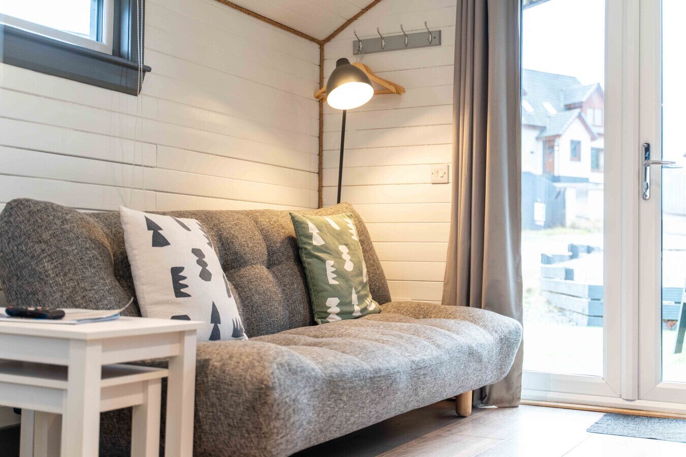 Una habitación acogedora con un sofá gris, una pequeña mesa blanca y una lámpara colgante.