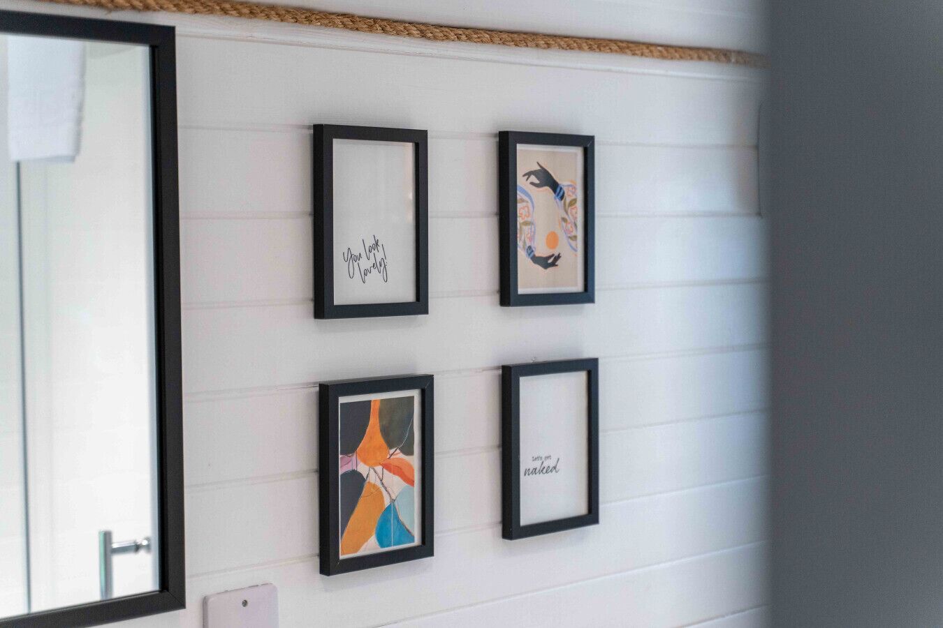 Four framed artworks on a white wall with horizontal paneling.