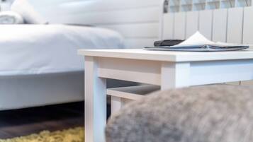 Una mesita de noche blanca con un teléfono inteligente y un libro en un dormitorio moderno con cama blanca y cabecera a rayas.