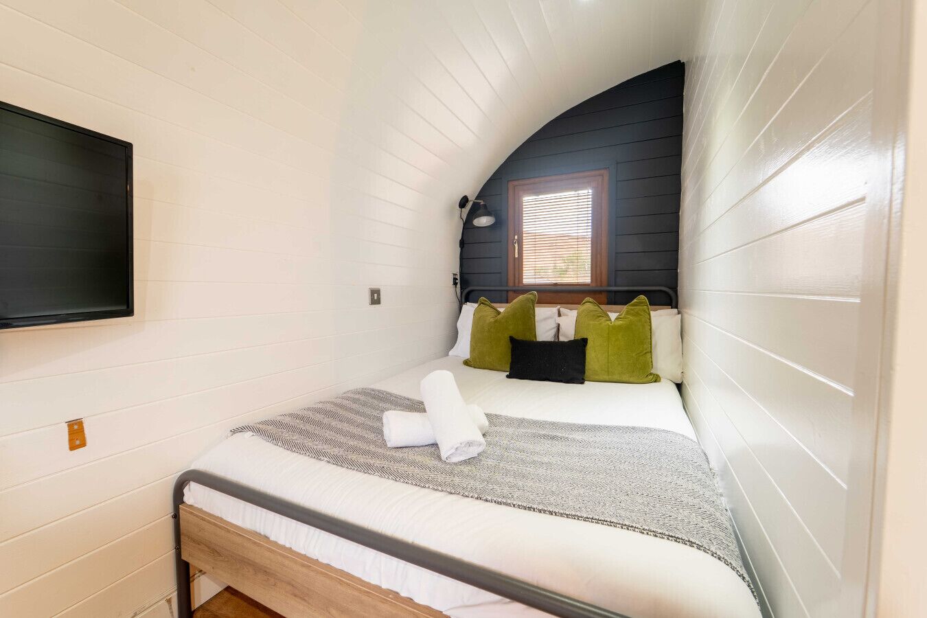 Een knus slaapkamer met een enkel bed, een flatscreen televisie aan de wand en een raam met luxaflex.