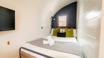 Een knus slaapkamer met een enkel bed, een flatscreen televisie aan de wand en een raam met luxaflex.