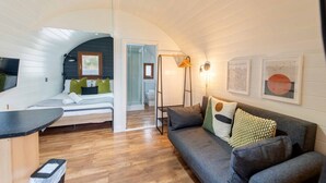 Une pièce compacte et bien éclairée, comprenant un lit, un canapé, une petite table et un espace douche.
