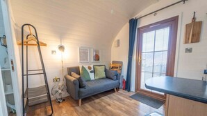 Un salon chaleureux avec un canapé gris, un plancher en bois, une échelle, un ventilateur et une fenêtre avec des rideaux.