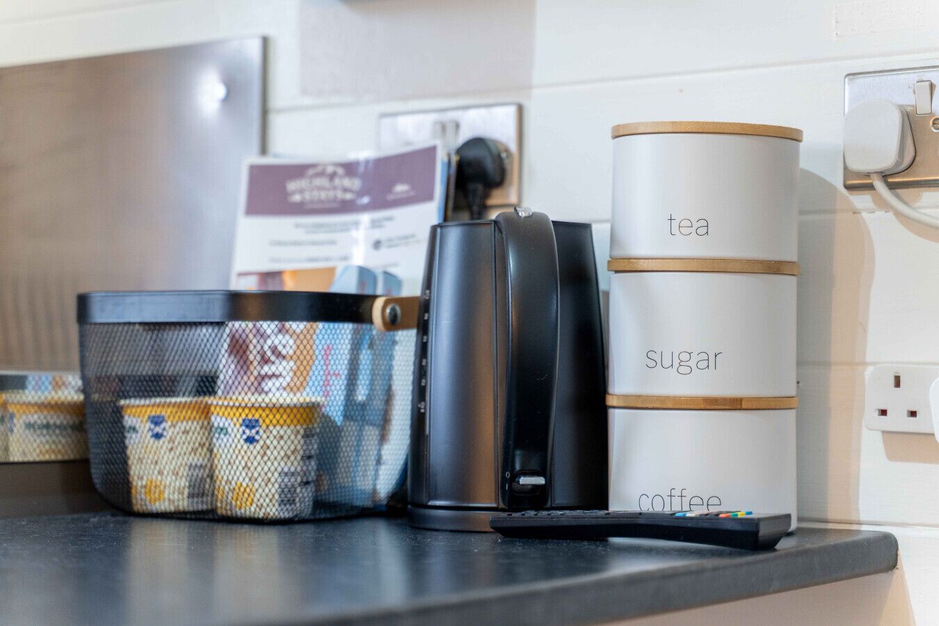 En köksbänk med en kaffebryggare, en tekanna med tillhörande tillbehör och en sockerskål.
