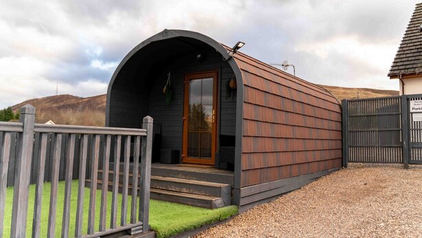 Une petite cabane moderne, dotée d’un toit incurvé et d’une porte en bois.