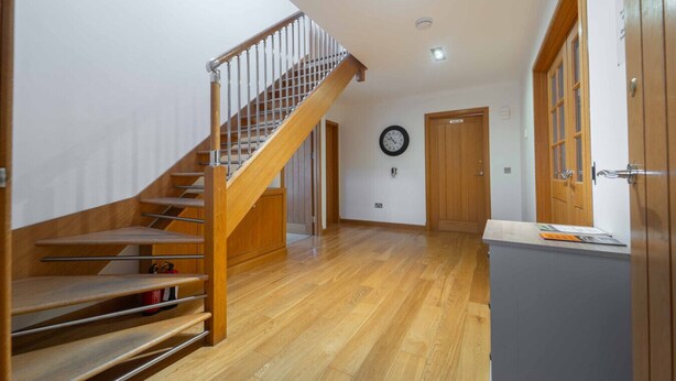 A spacious hallway with a wooden staircase, a clock on the wall, and a door with a window. - Ben View Room 2 in Fort William (Fort William)