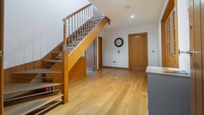 A spacious hallway with a wooden staircase, a clock on the wall, and a door with a window. - Ben View Room 3 in Fort William (Fort William)