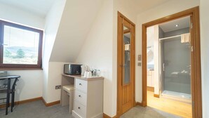 A small, well-lit room with a desk, a microwave, and a coffee maker. There is a door leading to a bathroom with a shower and a toilet visible. - Ben View Room 4 in Fort William (Fort William)