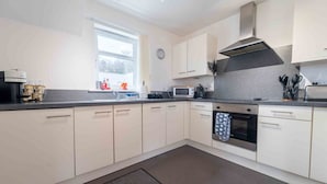 A modern kitchen with white cabinets, a microwave, oven, and a window with a view of trees.