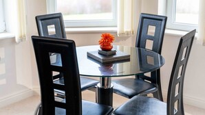 A round glass table with four black chairs, a small vase with a flower, and a stack of books.