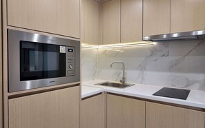 Une cuisine équipée d’un four à micro-ondes encastré, d’un évier en acier inoxydable et d’un dosseret en marbre.