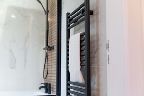 Une salle de bain avec un porte-serviettes noir sur lequel est posée une serviette blanche, une pomme de douche et un mur en marbre.