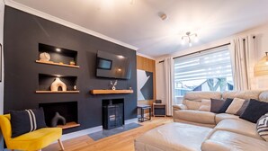Een moderne woonkamer met een bank, een gele fauteuil, een open haard en een aan de muur bevestigde televisie.