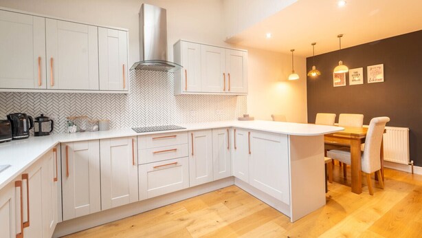 Een moderne keuken met witte kasten, een roestvrijstalen afzuigkap en een backsplash met een chevrond motief.