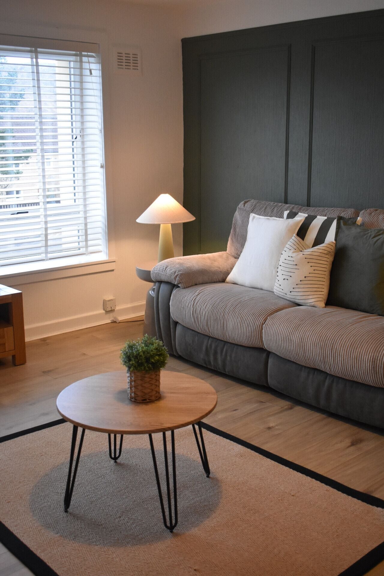 Un salon avec un canapé, une table basse ronde ornée d’une plante et une lampe.