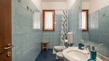 Un baño con azulejos azules, una puerta de madera, un inodoro, un lavabo y un taburete pequeño.