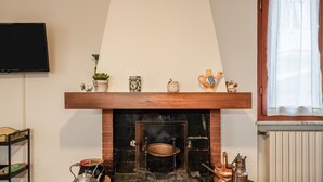 Een open haard met een bovenplaat waarop diverse decoratieve objecten staan, een aan de muur bevestigde televisie en een raam met gordijnen.