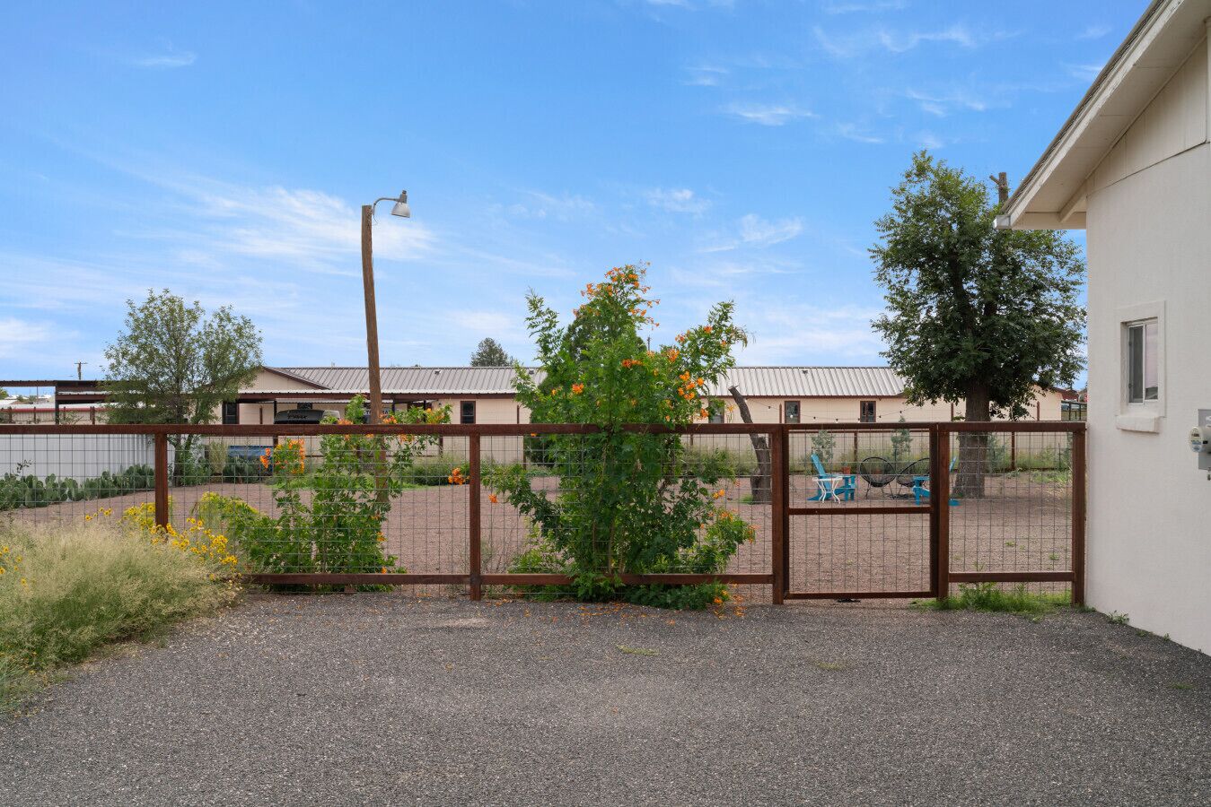 A fenced outdoor area with a gravel path, a metal gate, and a building in the background.