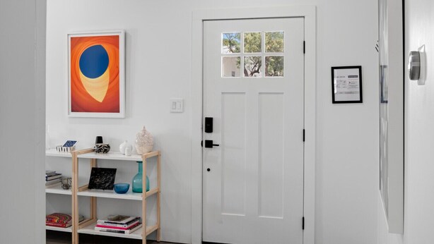 A white door with a small window, a framed abstract painting, and a shelf with books and decorative items. - The Art House in Marfa (Marfa)