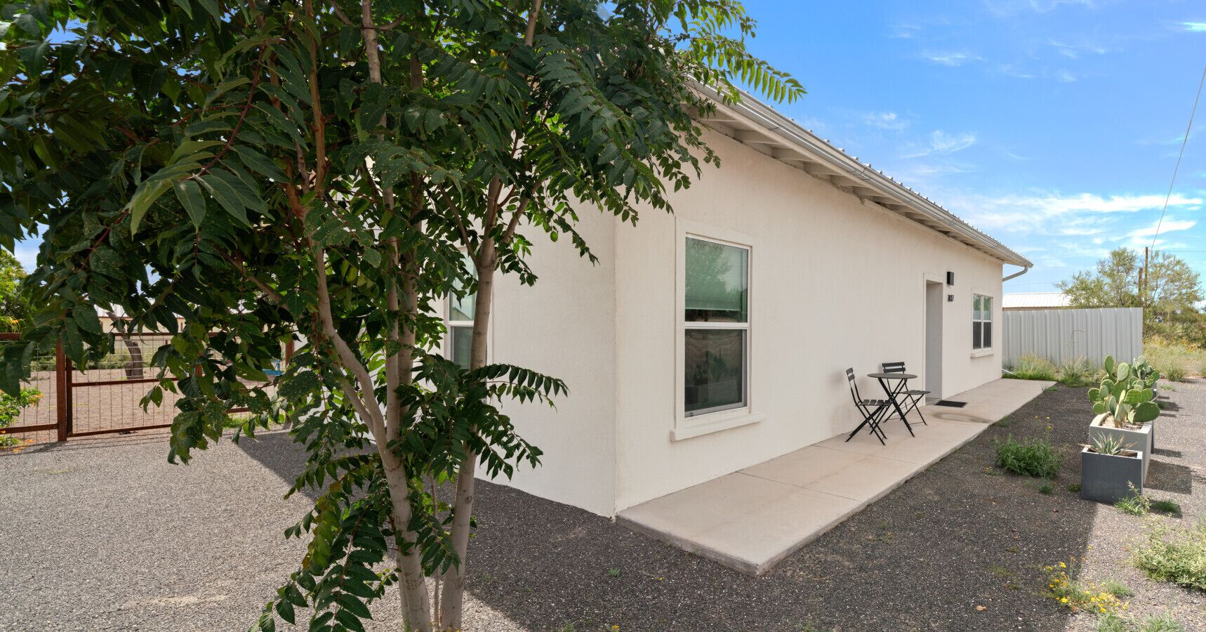 Un edificio moderno con un patio, una pequeña mesa y sillas, y una planta de cactus.
